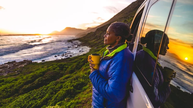 Image description: Woman stands next to car looking out at ocean.