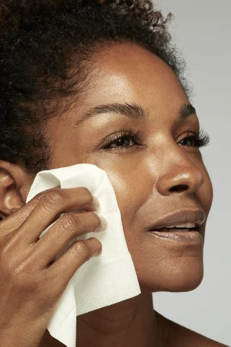 Beautiful woman holding a Prep-N-Glow wipe to her cheek.