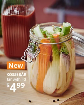 A vegetable-filled KÖSSEBÄR jar with lid sits on a wooden surface next to a bottle-shaped jar containing reddish juice.
