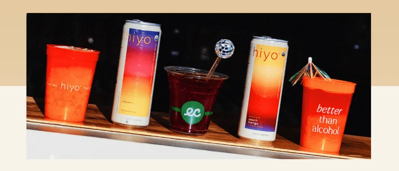 photo: hiyo blackberry lemon and peach mango cans sitting on bar beside mocktails.