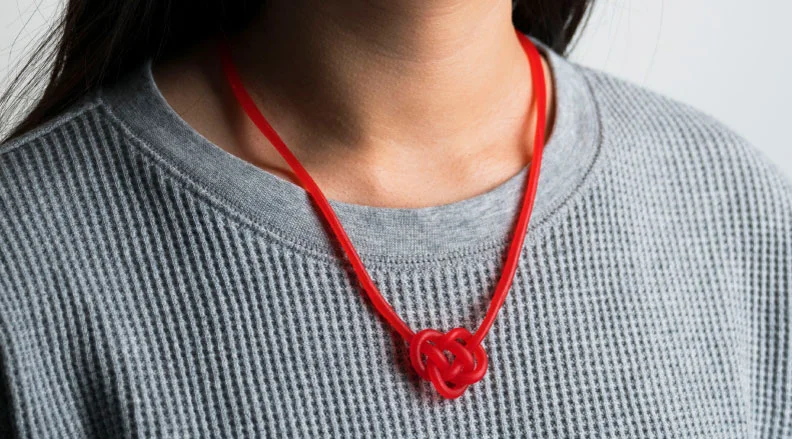 A person wearing a red licorice rope necklace in the shape of a Celtic heart knot.