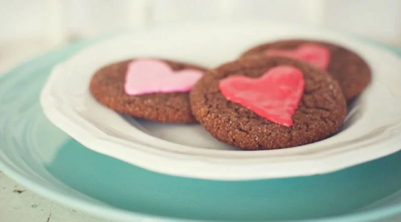 A plate of heart-shaped, red-iced ginger cookies alongside regular ginger crinkle cookies.