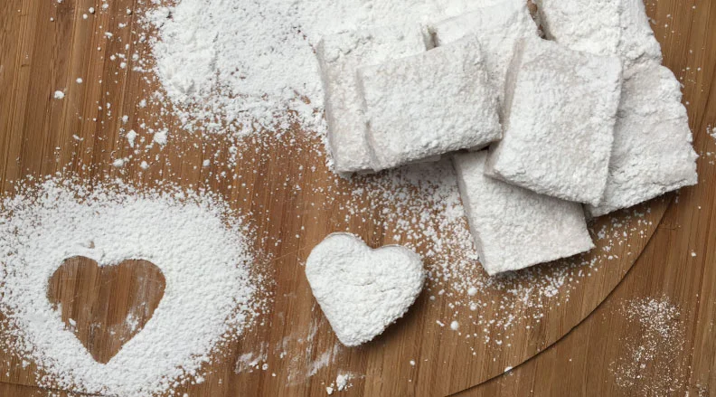 Powdered sugar-dusted marshmallows with a heart-shaped cutout on a wooden surface.