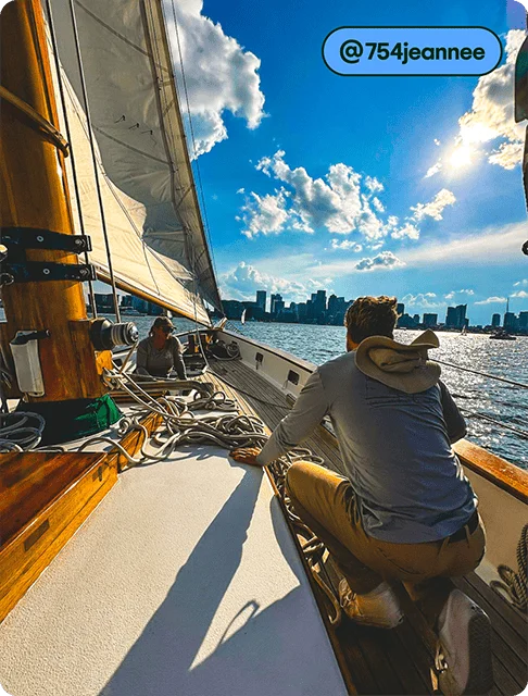 Image description: Two people are sitting on a sailboat, looking at the city skyline on a sunny day.