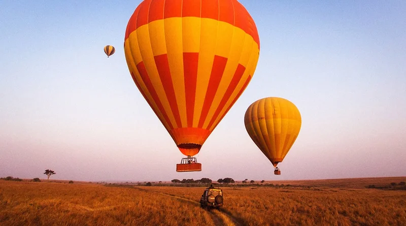 Image Description: Three hot air balloons flying over a field and a jeep driving down a dirt road.