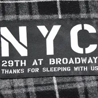 Close-up of Ace Hotel Shop blankets, including a cozy, checkered one with 'NYC 29th at Broadway' text.