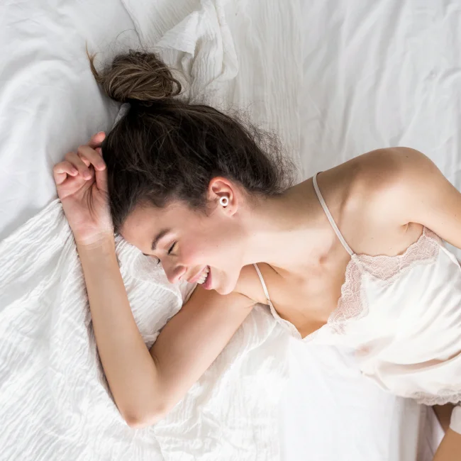A smiling woman relaxes in her bed.