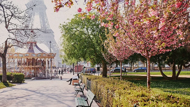 Image description: Flowering trees and merry-go-round in front of the Eiffel Tower, in Paris.