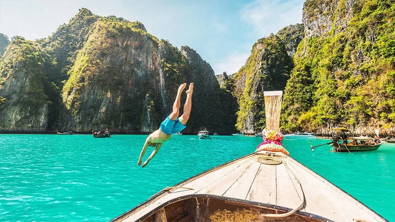Image description: Man jumping off boat into water at the Phi Phi Islands, in Thailand.