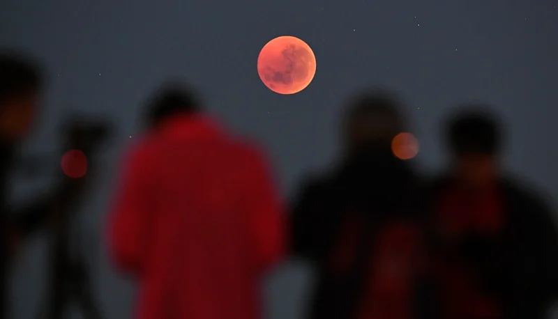 People gather to watch a “blood moon“ eclipse in Melbourne, Australia, on July 28, 2018. On March 13-14, 2025, skywatchers across North America will have a prime view as the Moon turns red during a total lunar eclipse—the first visible in the region since 2022.
