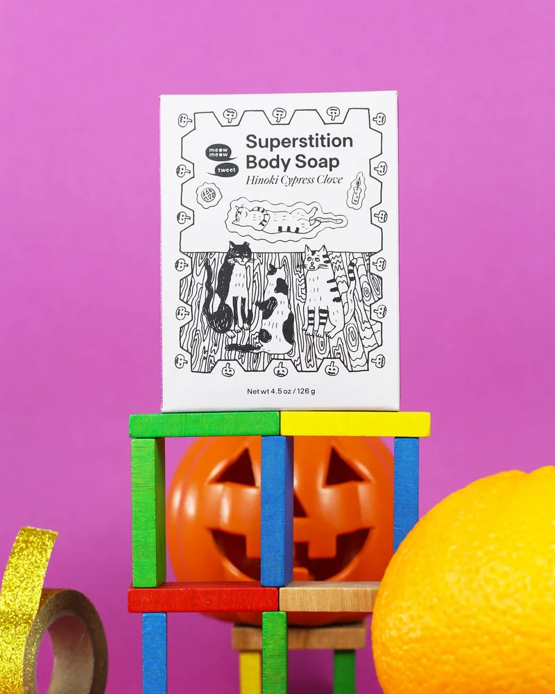 A grey-boxed bar of soap stnading on a stack of objects like a jackolantern, colored blocks, an orange, and golden tape