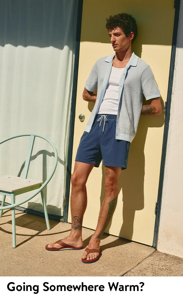 A man wearing a short-sleeve knit shirt over a tank and swim trunks.