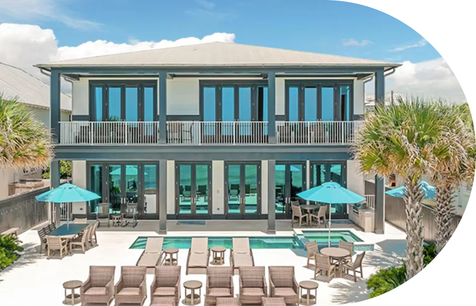 Two‑story coastal home with wide balconies, floor-to-ceiling windows, and private pool with sun loungers.