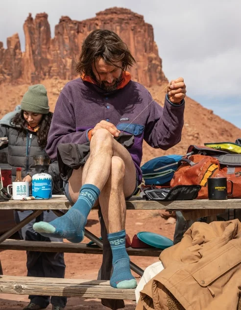 A person repairs a garment while sitting on a picnic table.