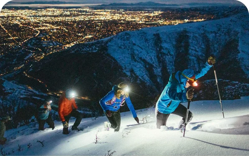 People hiking up a snowy mountain in the dark with headlamps on.