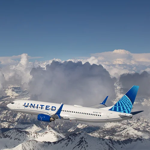 Image of United Airlines plane flying above snowy mountains.