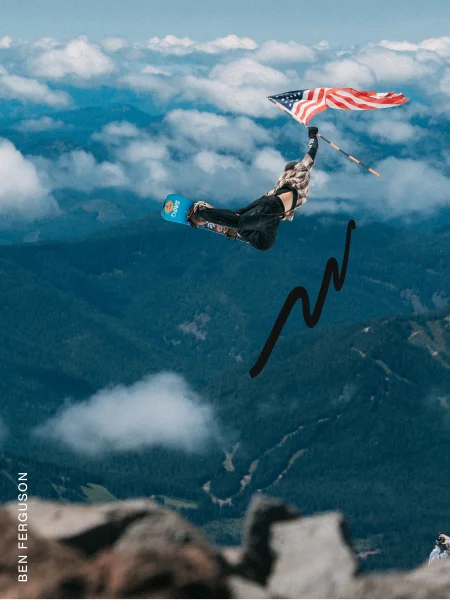 Burton athlete in the air riding the Burton Custom Snowboard in the mountains holding the flag of the US