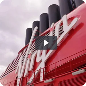 A play button overlaid on an image of a Virgin Voyages cruise ship funnel with the Virgin logo