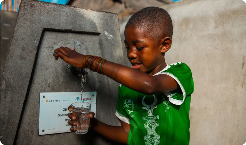 Boy in Madagascar filling a glass with clean water from a tap stand