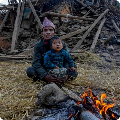 A Nepalis man and child with earthquake debris behind them.