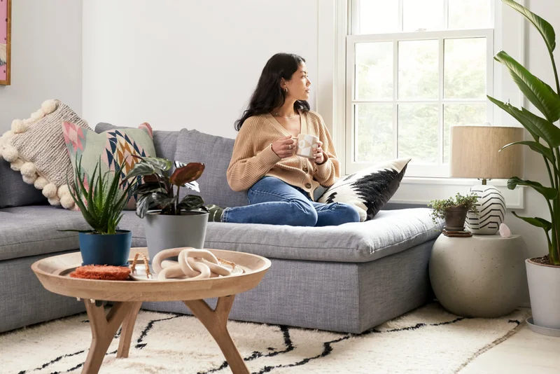 woman on couch and sipping coffee surrounded by plants