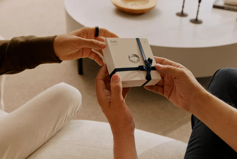 Hands exchanging a gift-wrapped Oura Ring box