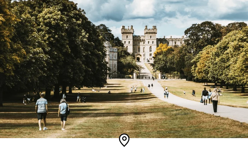 Image Description: Groups of travelers strolling through a park towards the gates of Windsor Castle in England, U.K.