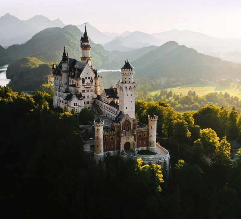 Image Description: An aerial shot of Neuschwanstein Castle surrounded by lush green forestry in the Bavarian Alps, Germany