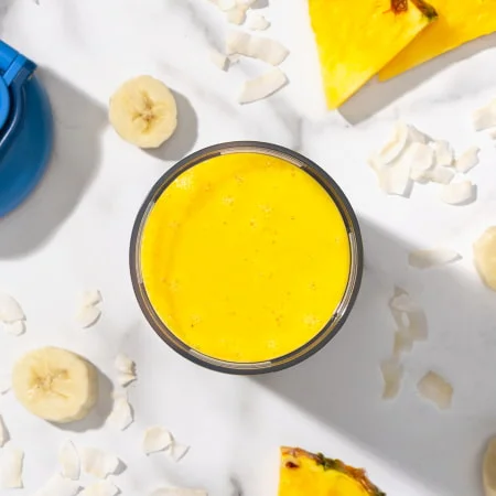 Bright yellow smoothie in a bowl, surrounded by pineapple and turmeric, representing a tropical anti-inflammatory recipe.