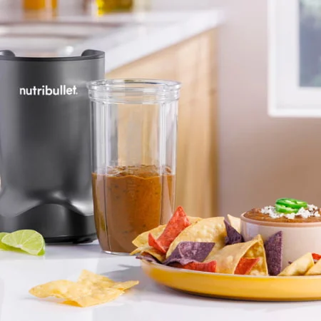 utribullet cup filled with blended black beans on countertop, next to a plate full of corn chips.