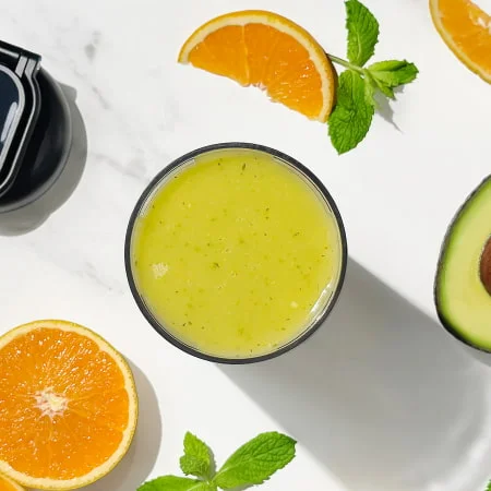Overhead view of a creamy green smoothie surrounded by fresh mint and lime slices, promoting a refreshing and calming drink.