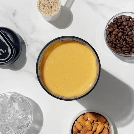 A rich, coffee-colored smoothie in a glass next to coffee beans and ice, highlighting a protein-packed cold brew blend.
