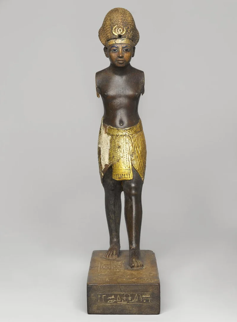 Black and gold wooden figure standing on a rectangular base with left foot forward