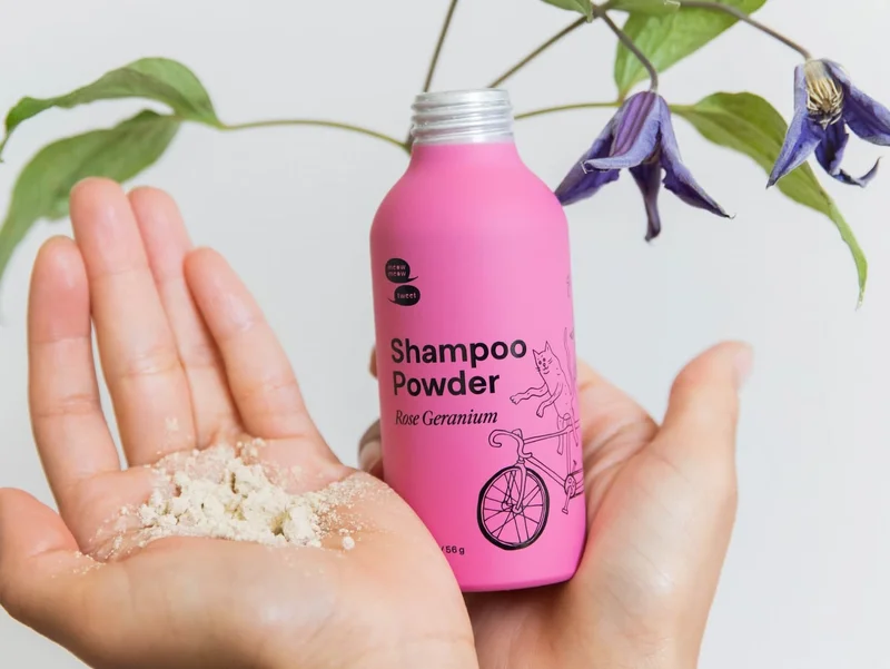 A pair of hands hold up a pink bottle of shampoo powder in one hand and a pile of the powder in the other.