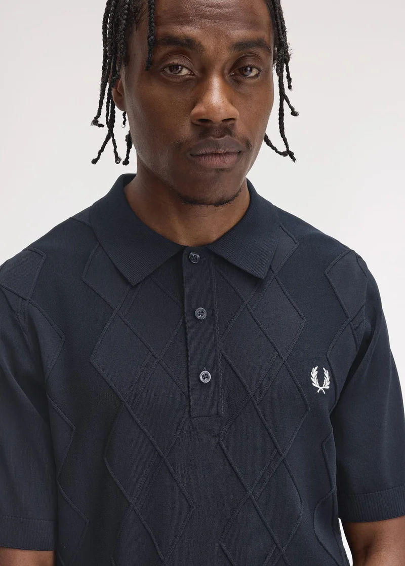 Black model with twists wears textured knitted navy polo with diamond detailing