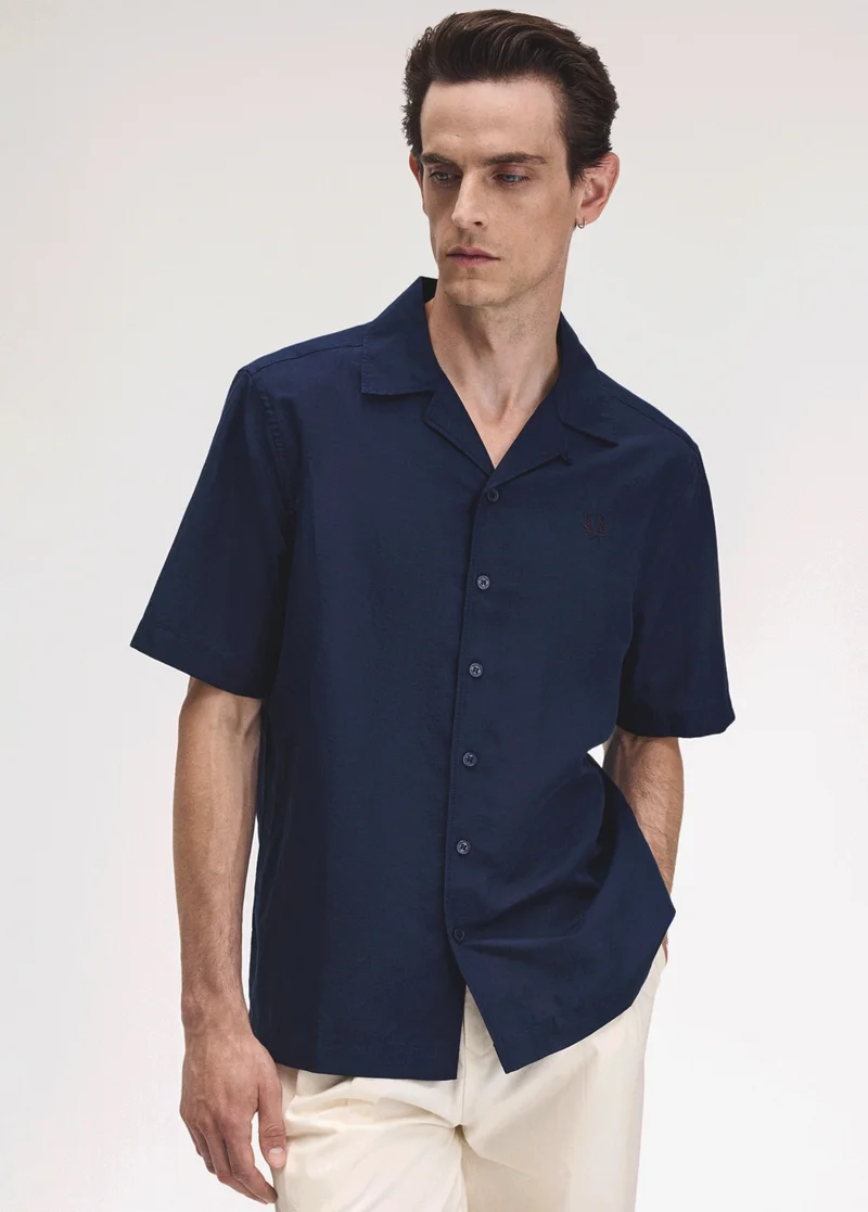 White male model with coiffed hair stands relaxed in a revere collar short-sleeved shirt in navy