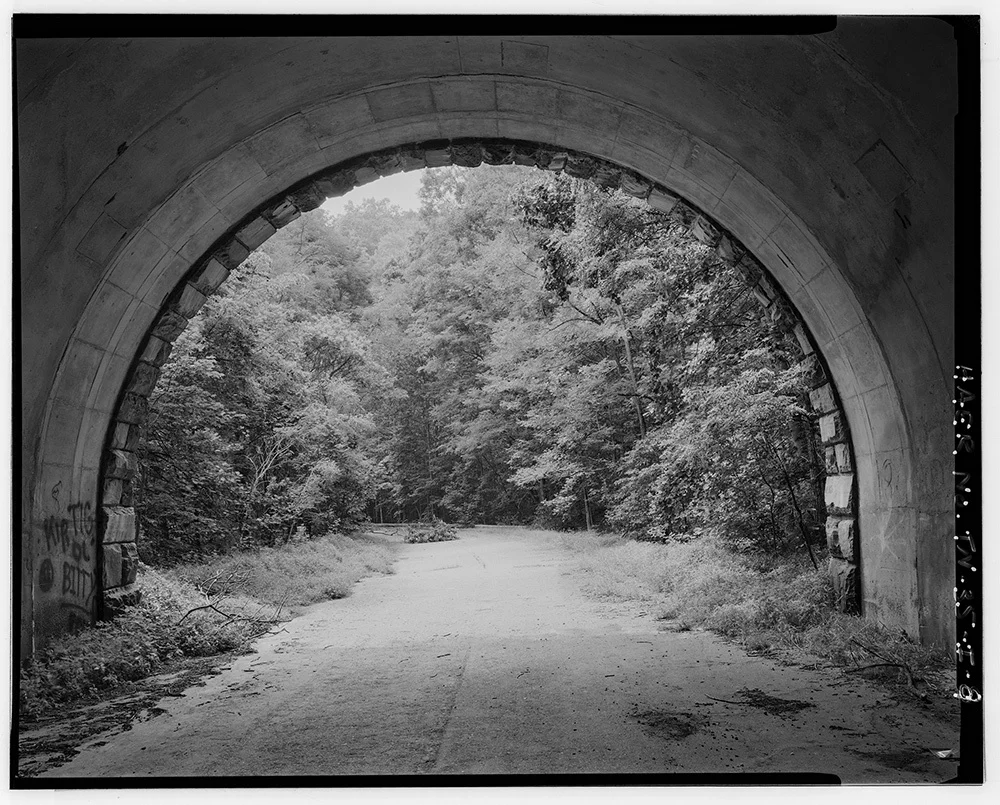 Black and white image of the end of the tunnel looking out.