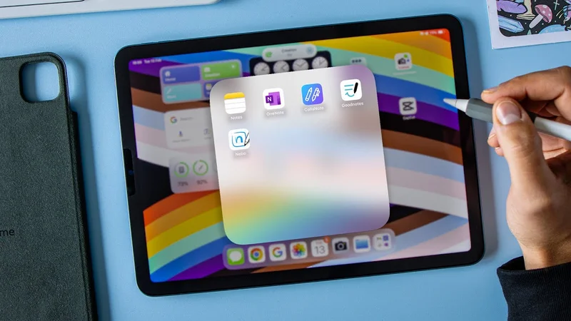 An iPad sits on a blue background with icons for notetaking apps on the screen. A hand off to the right holds an Apple Pencil with Paperlike’s Pencil Grip on it.