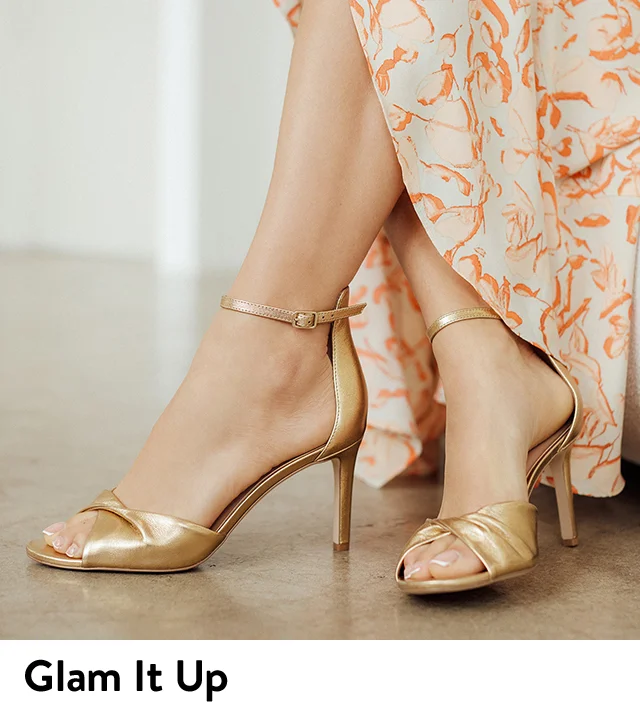 A woman wearing an orange and white dress and gold heels.