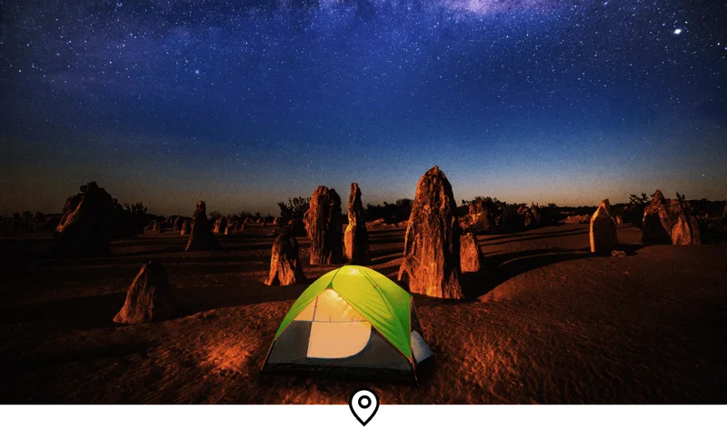 Image Description: A glowing green tent in the Pinnacles Desert on a dark, starry night, with a clear view of the Milky Way above