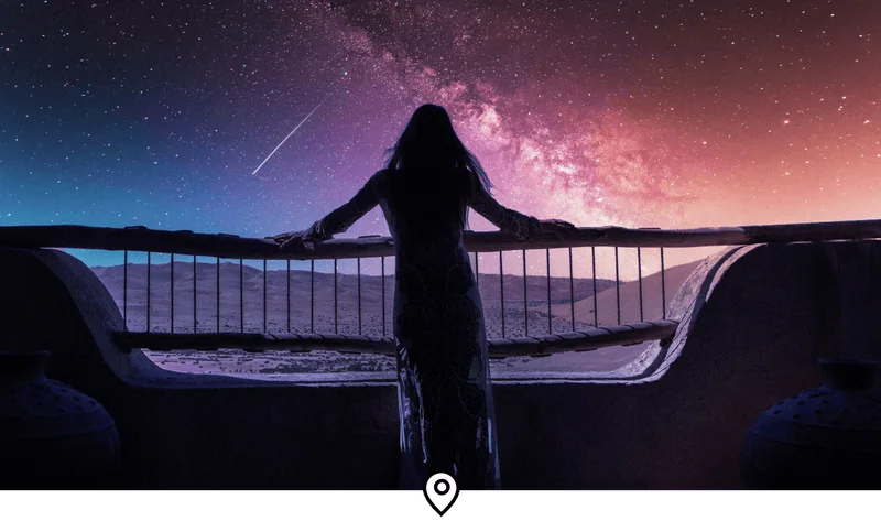Image Description: A woman admiring a shooting star on her hotel balcony in the middle of the Arabian Desert