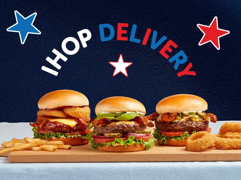 A photo of three IHOP Steakburgers on a cutting board, flanked by fries and onion rings.