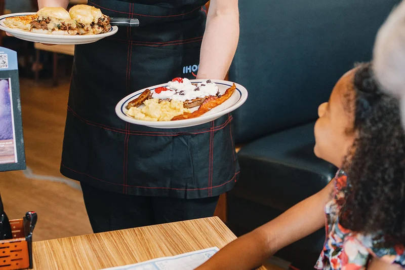 An IHOP server hands a child seated at a booth the Happy Face kids meal.