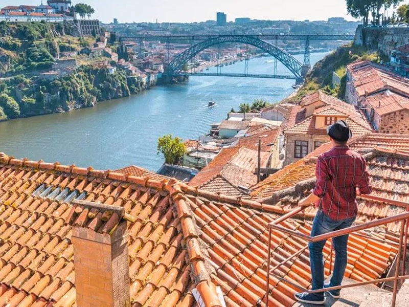 Rooftop view over river and bridge in Porto with person in foreground.
