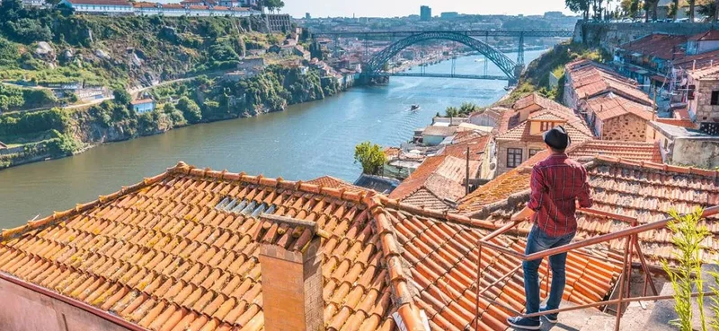 Rooftop view over river and bridge in Porto with person in foreground.