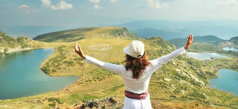 Woman with oustretched arms in foreground of view over Seven Rila Lakes.
