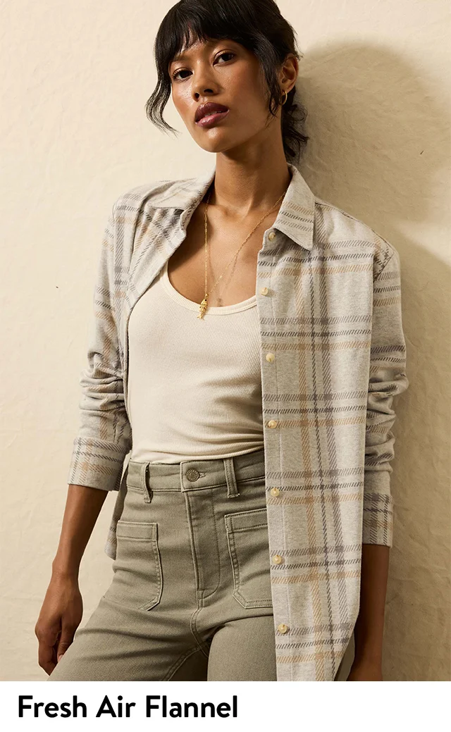 A woman wearing a flannel top with a ribbed tank and jeans.