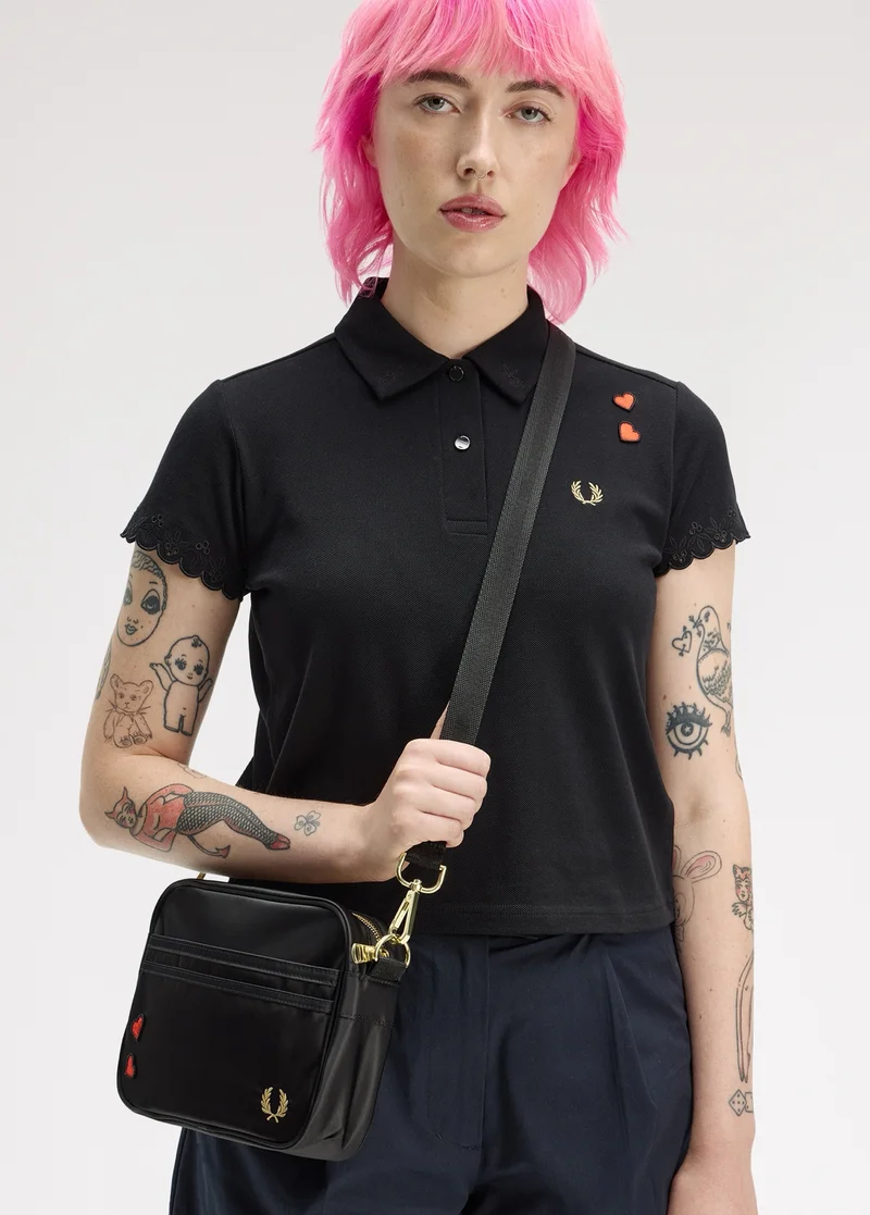 Female model wearing a Fred Perry x Amy Winehouse Foundation Embroidered Detail Polo Shirt in Black and Mini Shoulder Bag