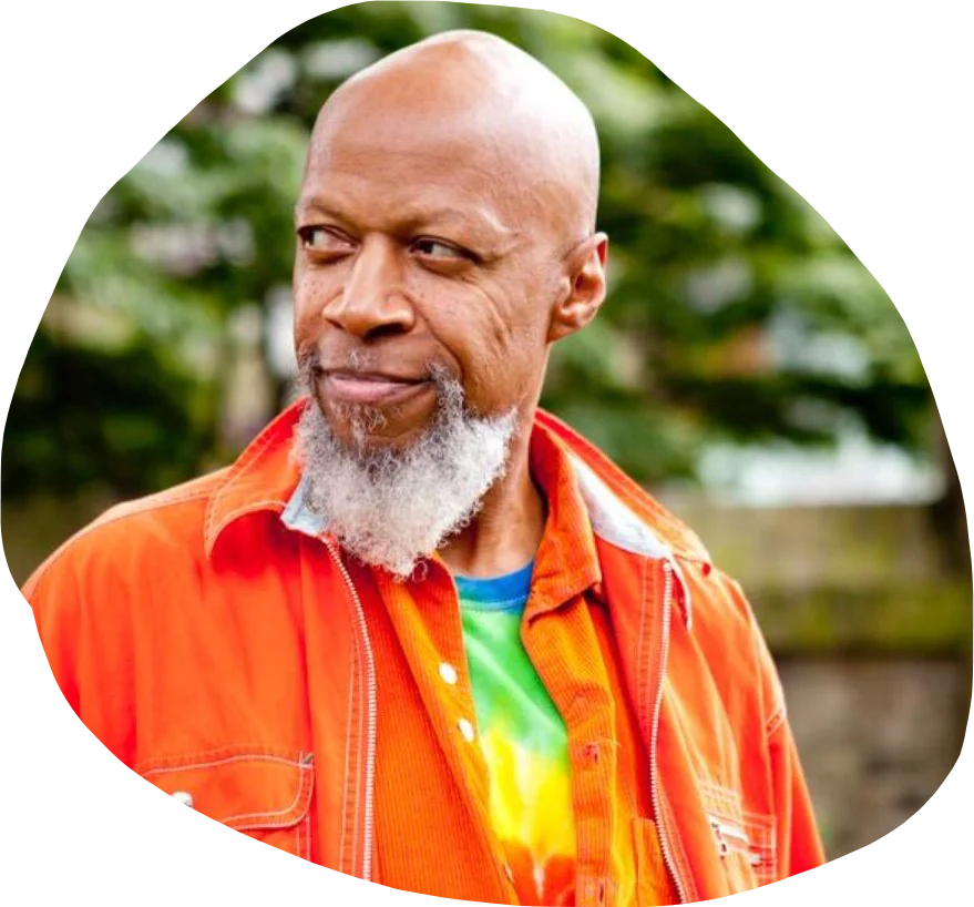 A man with a beard in a bright orange coat stares to the side, smiling softly