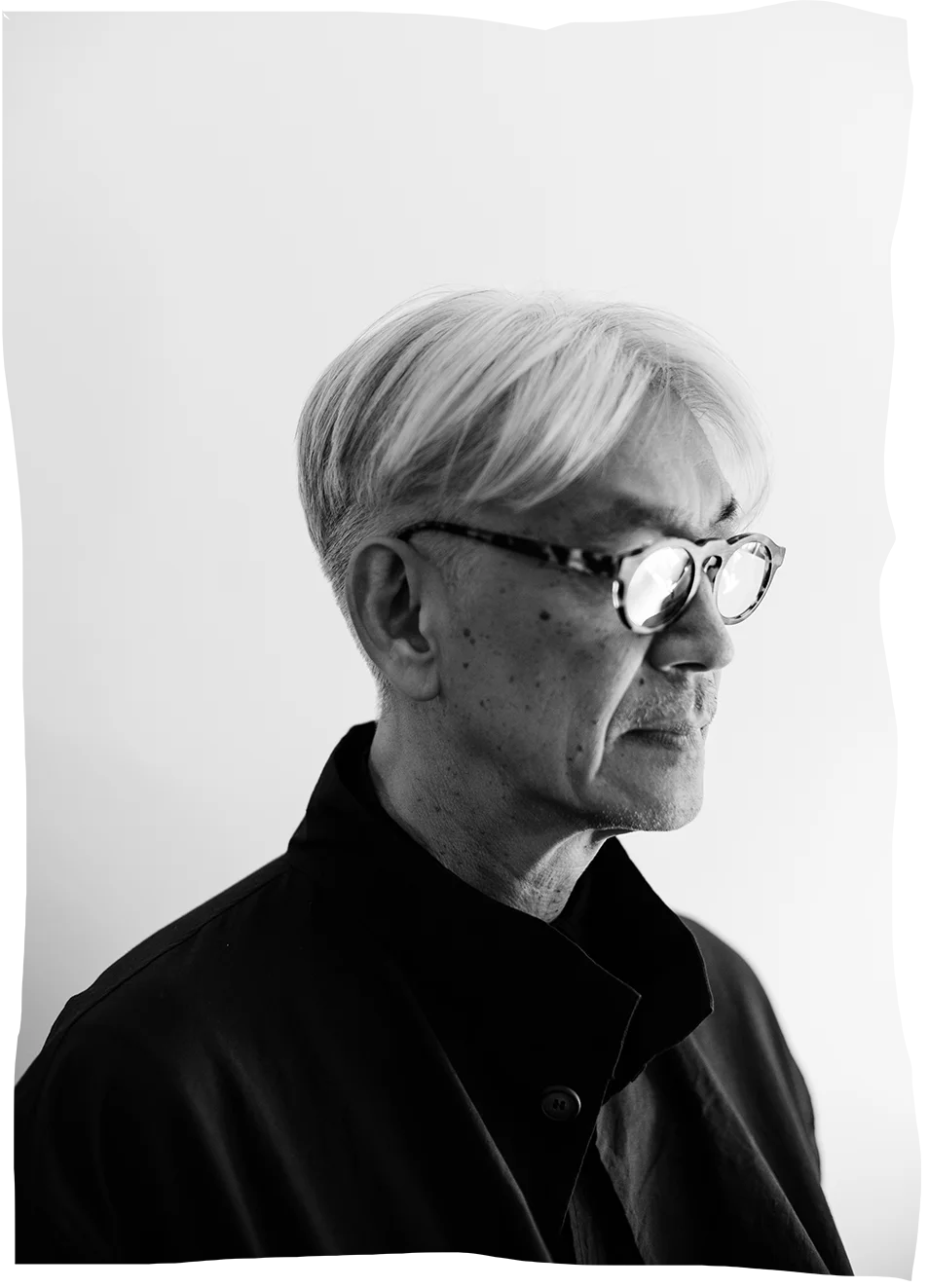 A man with white hair and glasses stares pensively to the right